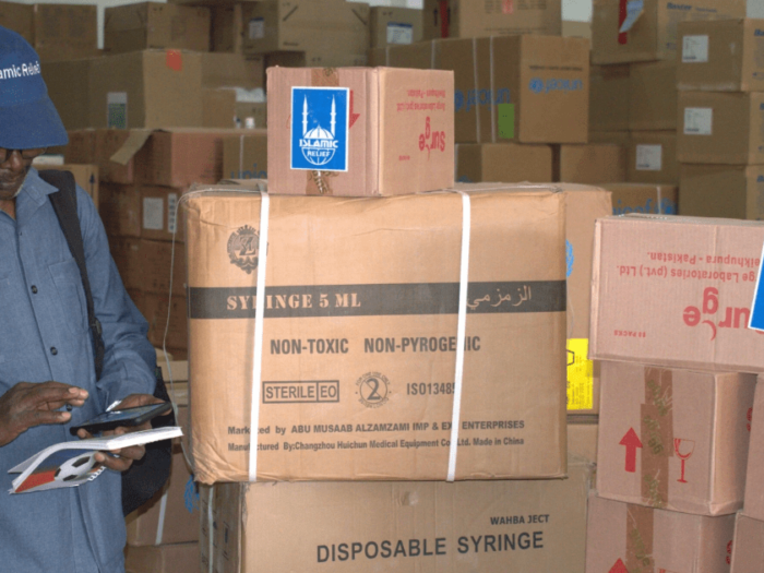 a man standing infront of a stack of boxes in a warehouse with medical supplies for sudan