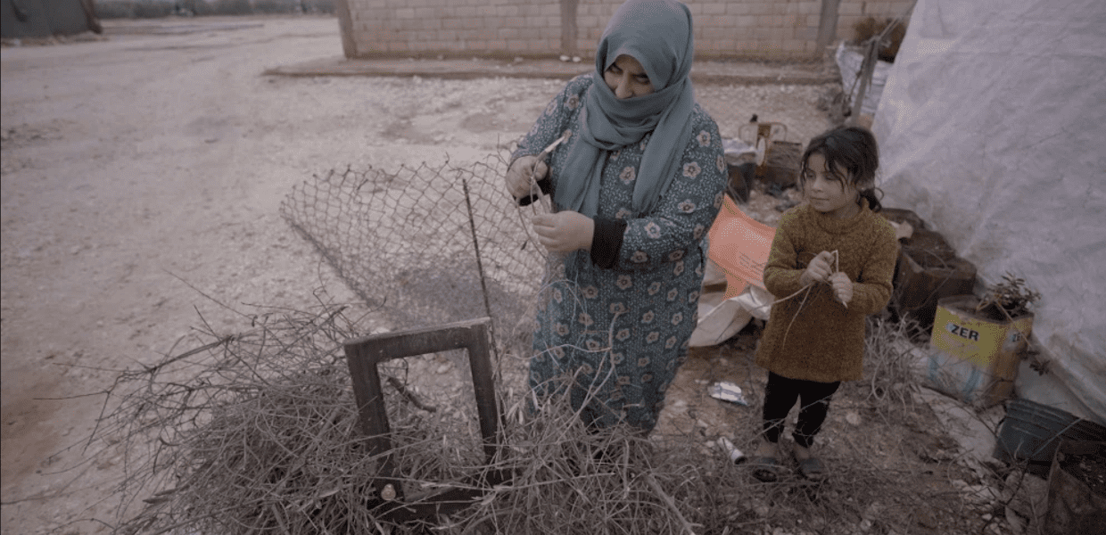 a syrian mother and daughter in a camp gathering twigs and bits of wood